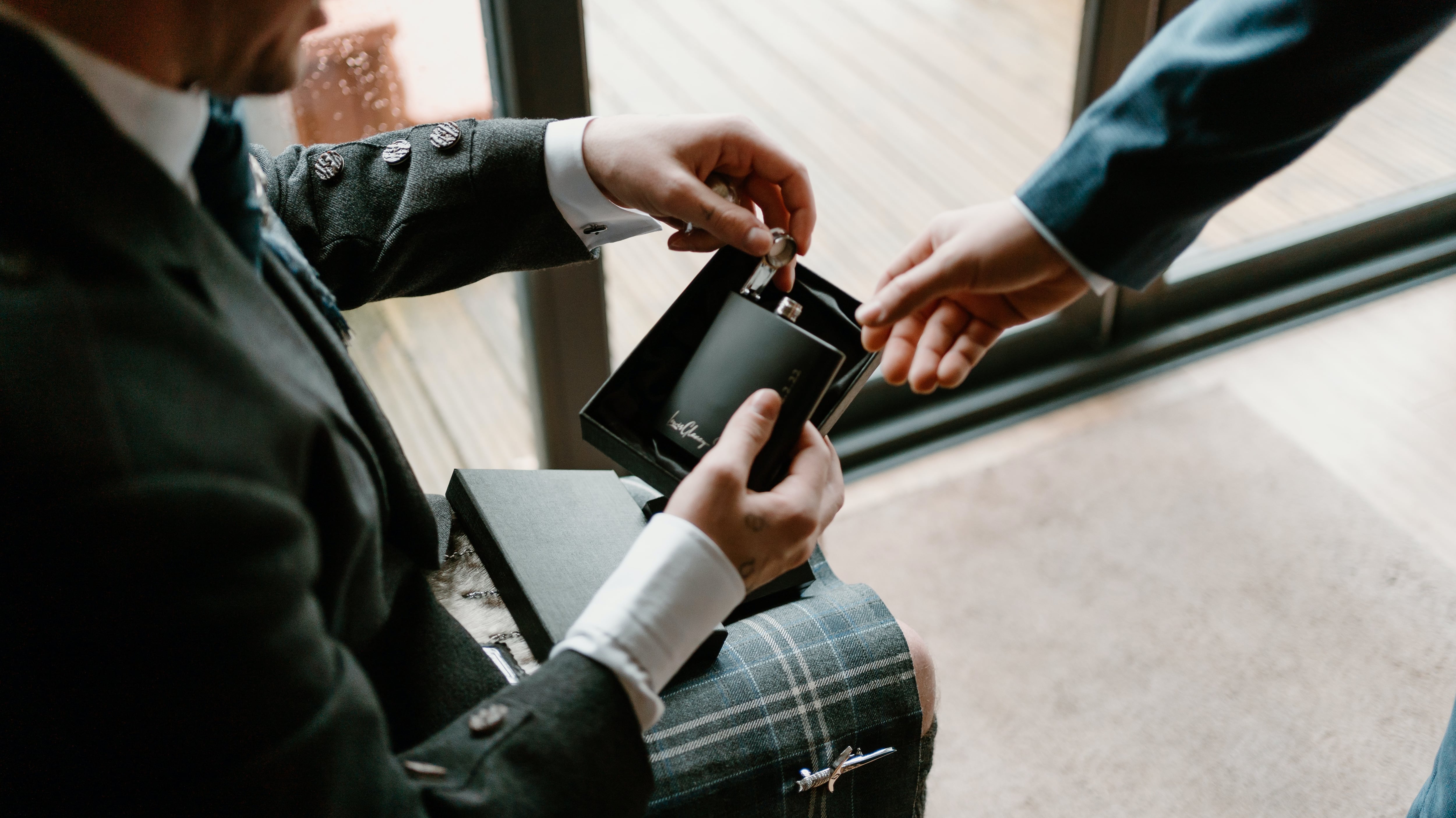 Homem de terno e saia escocesa segurando frasco de perfume