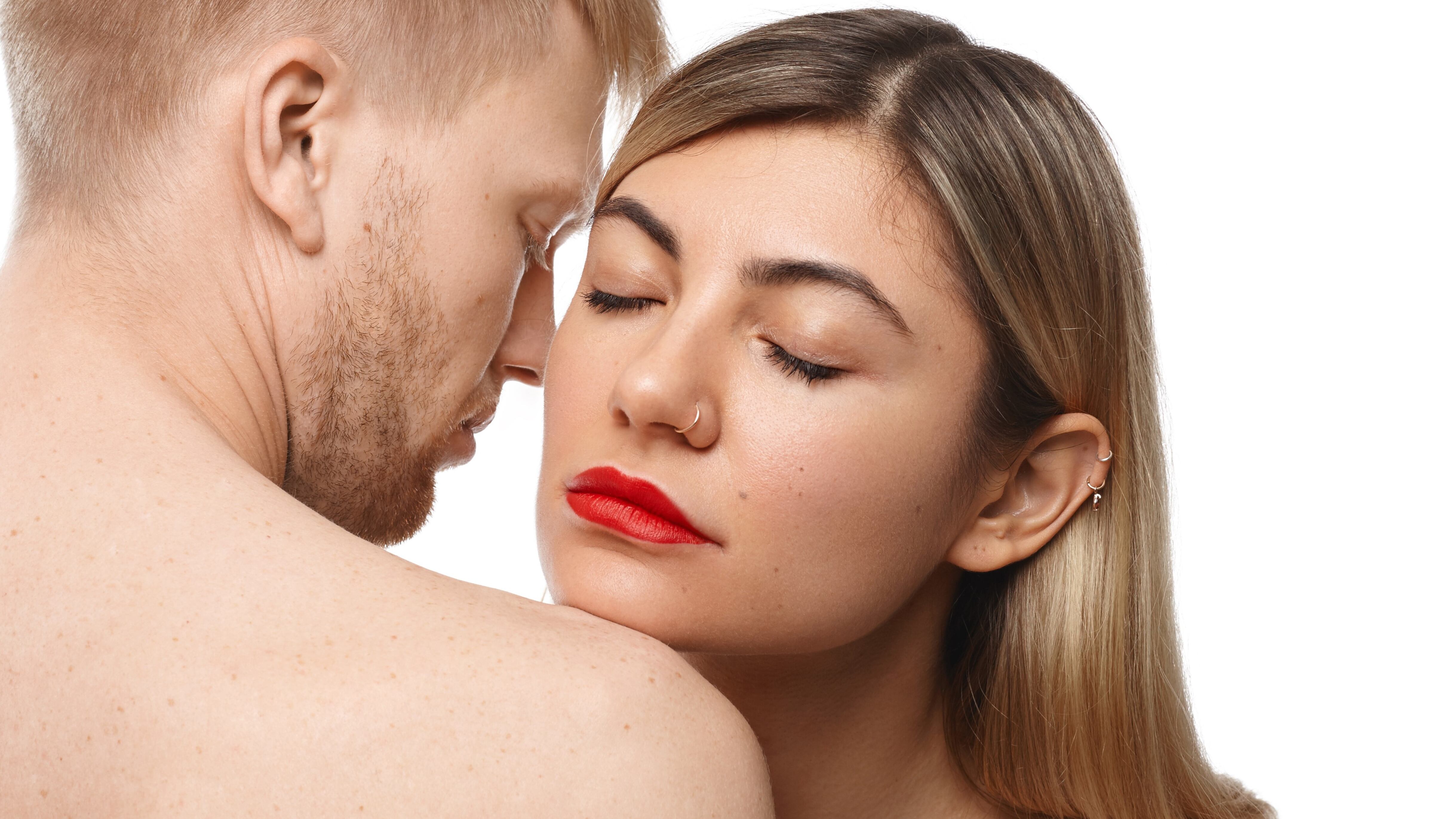 Mulher branca de batom vermelho cheirando pescoço de homem branco loiro sem camisa