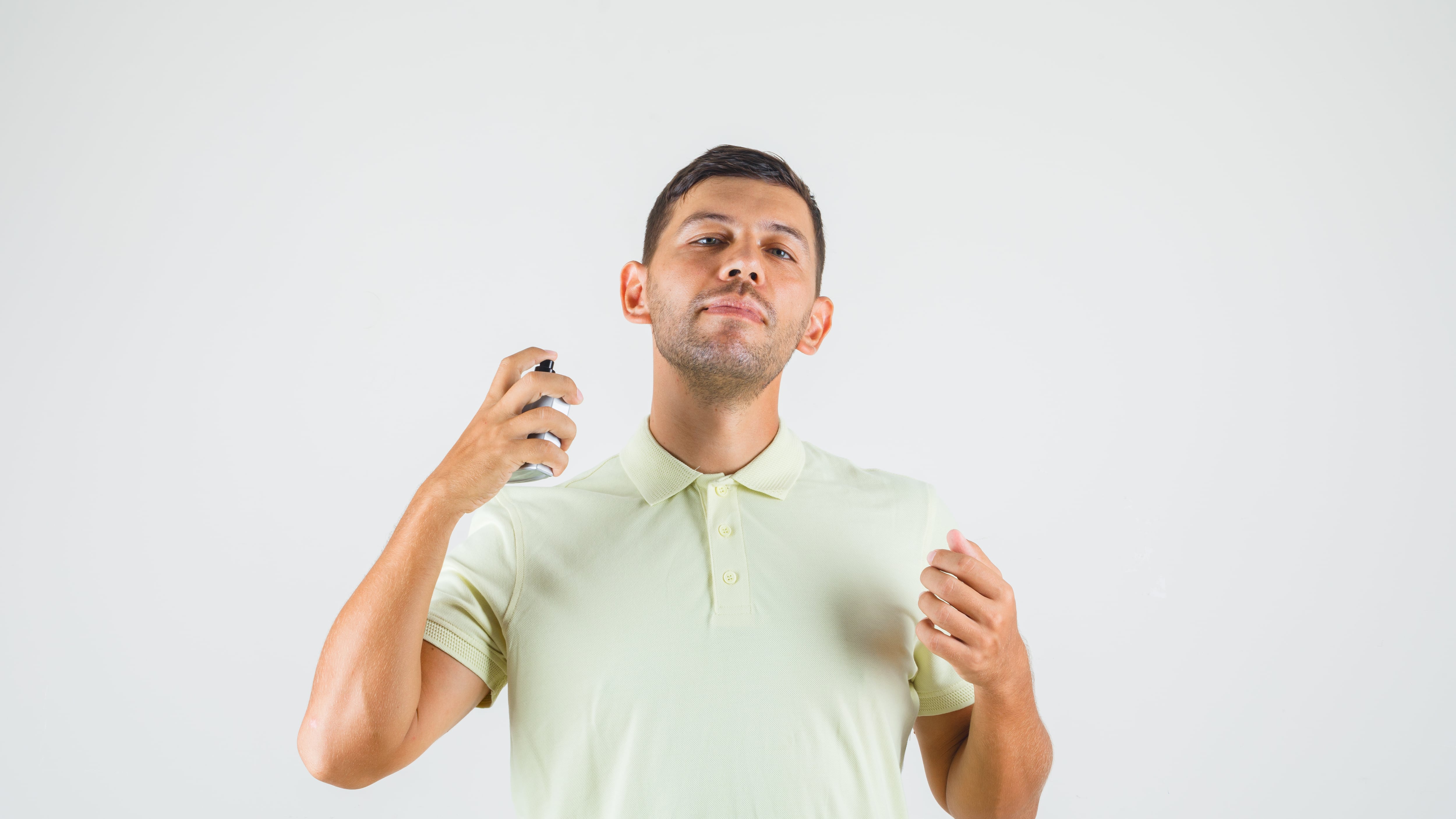 Young man applying perfume on his neck in t-shirt front view.