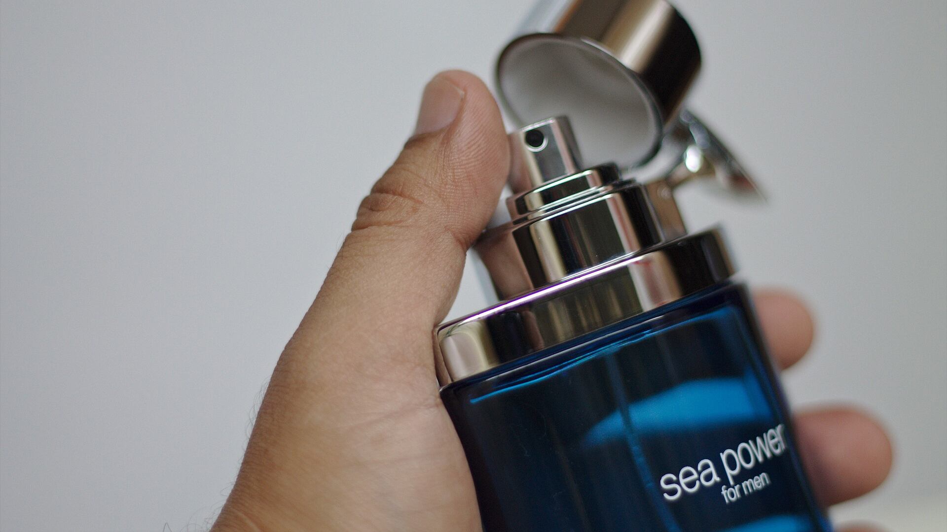 Silhueta de mão masculina segurando frasco de perfume azul