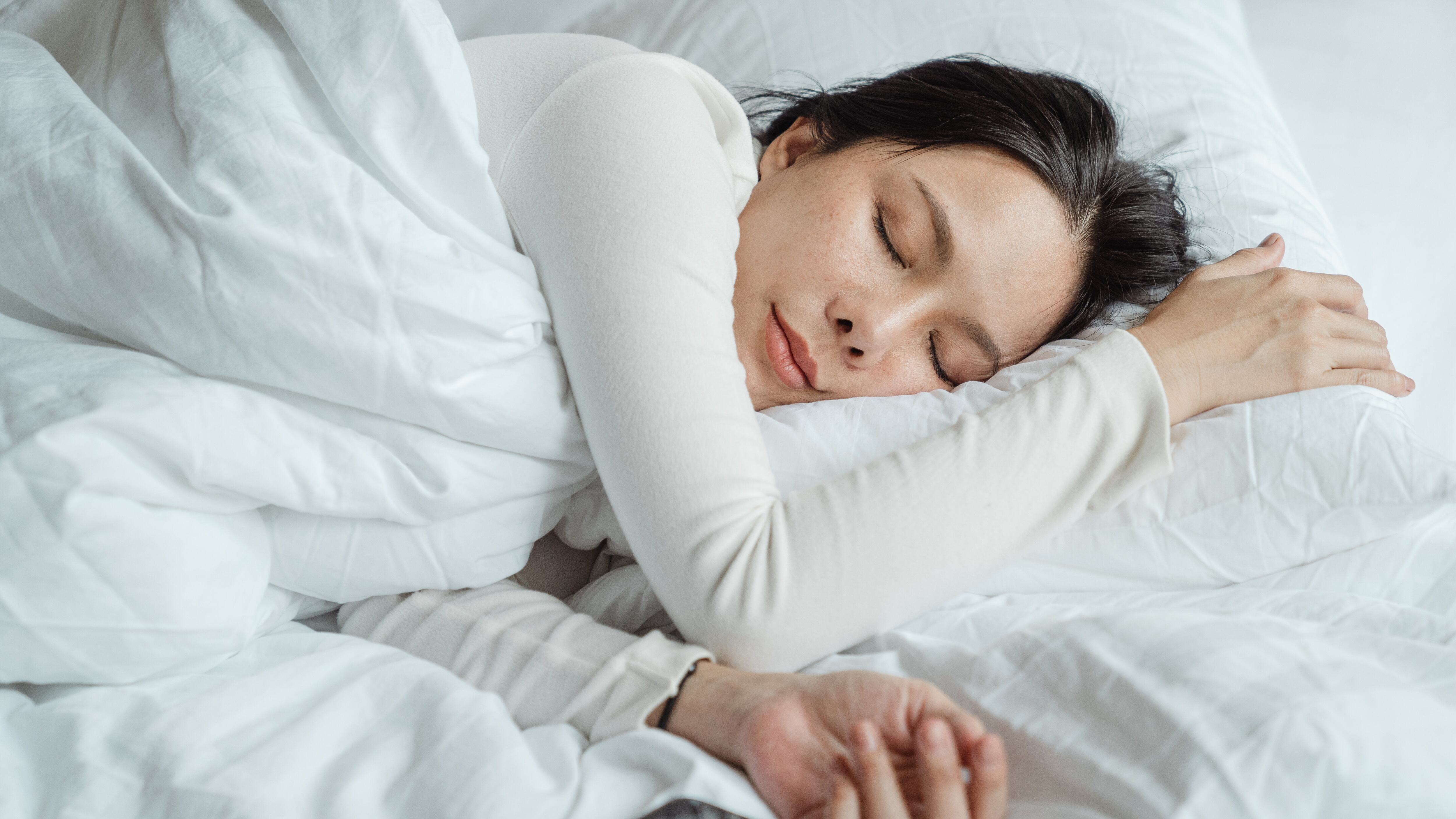 Mulher asiática dormindo ao lado de celular com roupas de cama branca