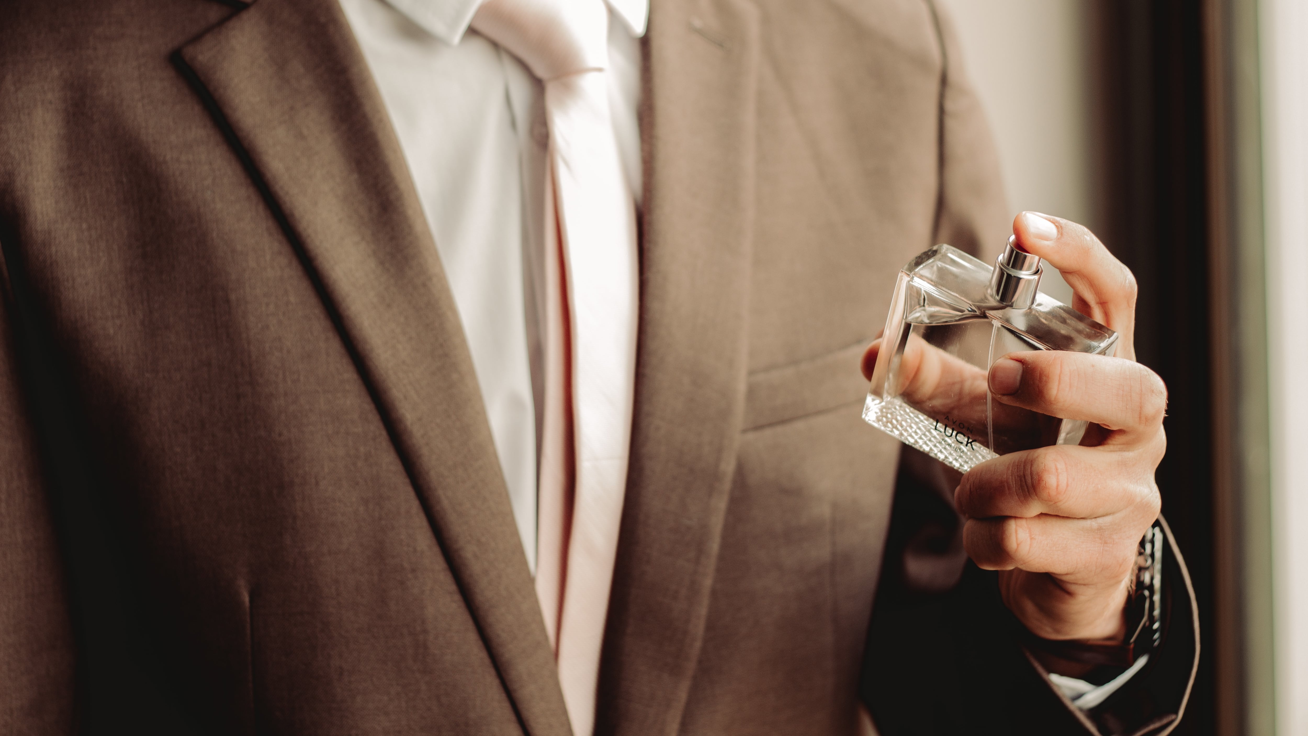 Homem de terno marrom borrifando perfume
